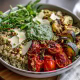 A close-up of the Arugula Pesto Bowl reveals shaved Parmesan and golden pine nuts over colorful roasted vegetables and grains.