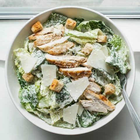 Freshly made Chicken Caesar Salad tossed in a wooden bowl, served with extra dressing on the side for dipping.