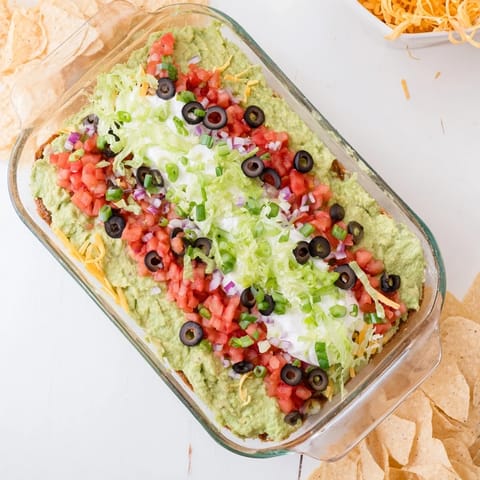 A chilled Tex-Mex dip featuring vibrant layers of beans, salsa, olives, lettuce, and green onions.