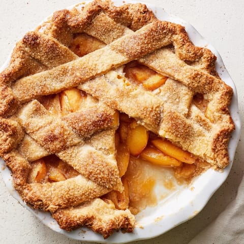 Warm Peach Pie is served with a scoop of melting vanilla ice cream on a white dessert plate.