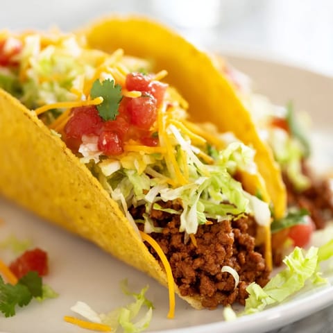 Golden beef tacos with seasoned meat topped with shredded lettuce, cheddar cheese, and fresh salsa.
