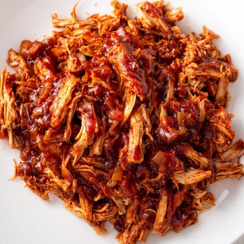 Shredded BBQ Pulled Chicken piled high on toasted buns, garnished with crisp pickles and creamy coleslaw for dinner.