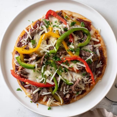 A close-up of Philly Cheesesteak Pizza topped with gooey cheese blend, tender steak, and vibrant bell peppers on a wooden board.