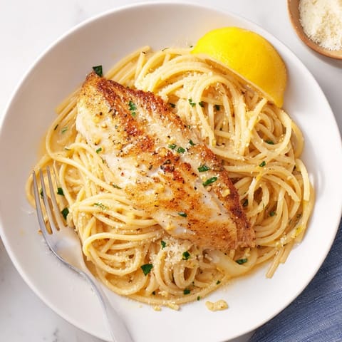 A close-up view of tender white fish and zesty lemon pasta, highlighting the vibrant colors and fresh herbs on a rustic wooden table.  