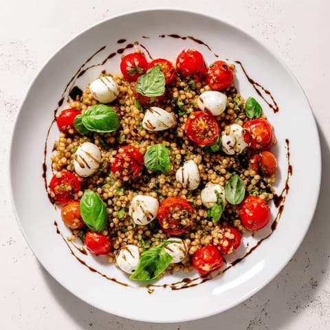 Vibrant Caprese Couscous Salad tossed with juicy tomato halves, creamy mozzarella, and fragrant basil on a serving platter.