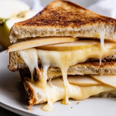 Close-up of a gooey smoked Gouda and apple grilled cheese sandwich on a plate, perfect with a side of tomato soup.