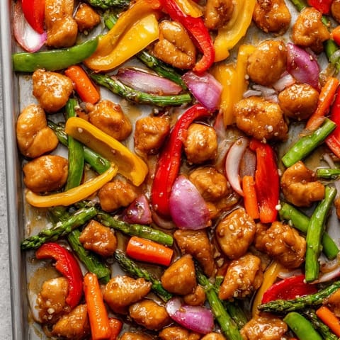 Golden-brown chicken and vibrant spring vegetables coated in a glossy honey garlic sauce, roasted together on a single sheet pan.  