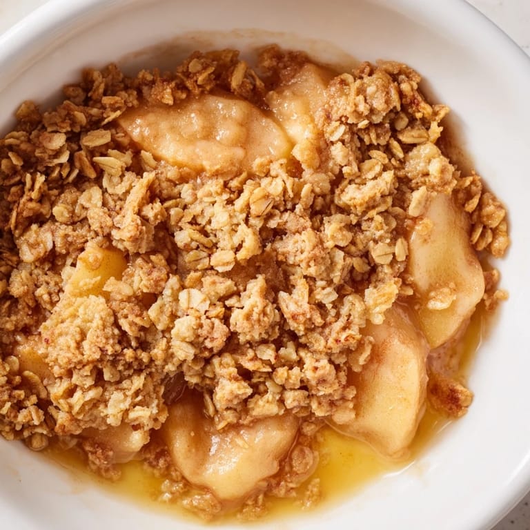Serving of Apple Crumble topped with vanilla ice cream melting over tender, spiced apples in a rustic bowl.
