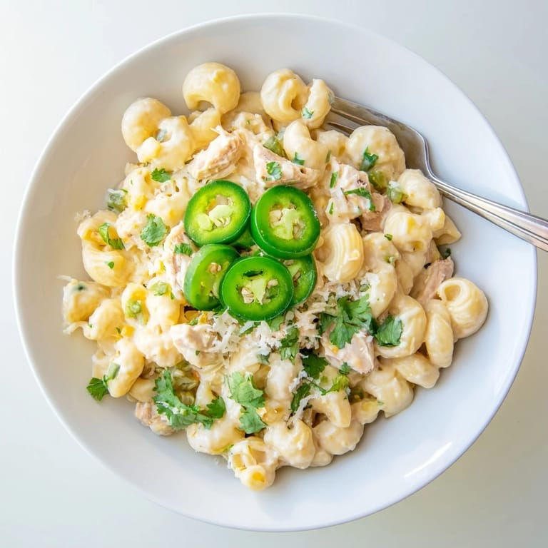 A spoon lifts a cheesy serving of Green Chili Chicken Mac from the skillet, revealing tender chicken and diced green chiles.