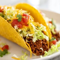 Golden beef tacos with seasoned meat topped with shredded lettuce, cheddar cheese, and fresh salsa.