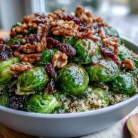 A vibrant Roasted Brussels Sprouts Bowl with caramelized sprouts and onions over fluffy quinoa, topped with toasted walnuts and dried cranberries.
