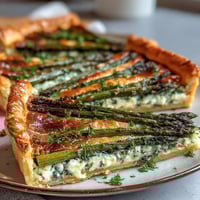 A golden puff pastry tart topped with fresh spring asparagus, creamy cheese, and herbs—perfect for brunch or a light vegetarian meal.
